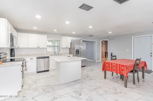 a large kitchen with kitchen island a sink white cabinets and stainless steel appliances
