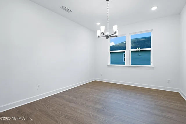 a view of empty room with wooden floor and chandelier