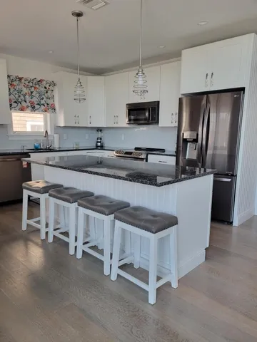 a kitchen with stainless steel appliances granite countertop a stove a sink dishwasher a refrigerator and white cabinets with wooden floor