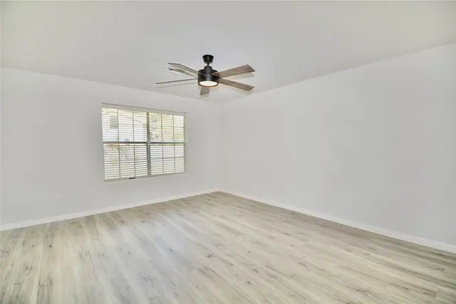 an empty room with wooden floor fan and windows