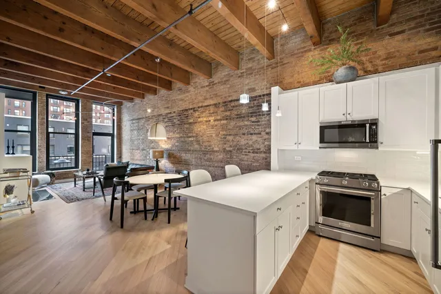 a kitchen with stainless steel appliances a stove a sink a microwave oven a dining table and chairs with wooden floor