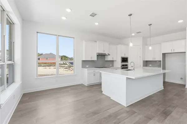 a kitchen with stainless steel appliances granite countertop a stove a sink a refrigerator and white cabinets with wooden floor