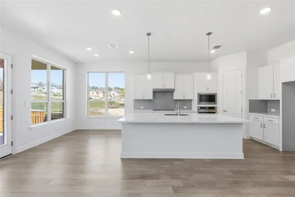 a large white kitchen with stainless steel appliances granite countertop a stove a sink a refrigerator white cabinets and wooden floor next to a window