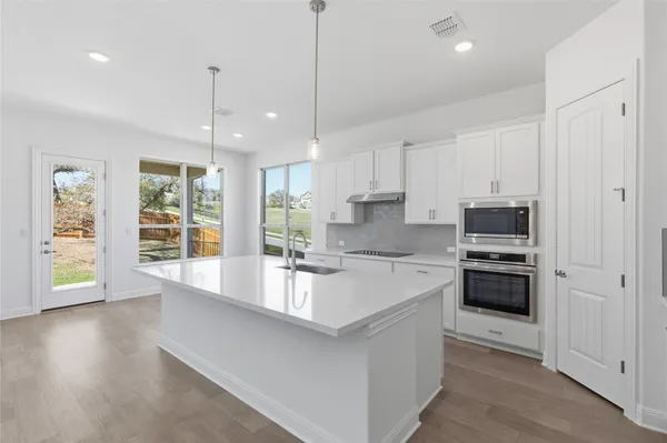 a large white kitchen with a stove a refrigerator a oven a sink with a dining table and chairs