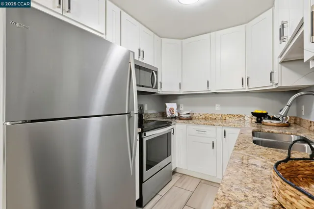 a kitchen with stainless steel appliances granite countertop a refrigerator a stove a sink and white cabinets