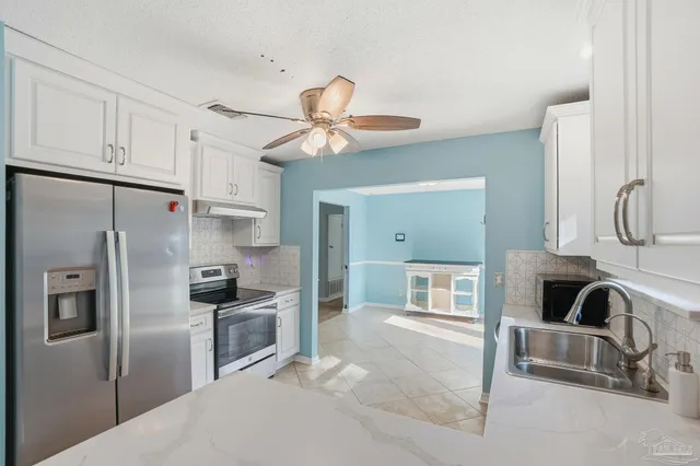 a kitchen with stainless steel appliances granite countertop a refrigerator a sink a stove and white cabinets