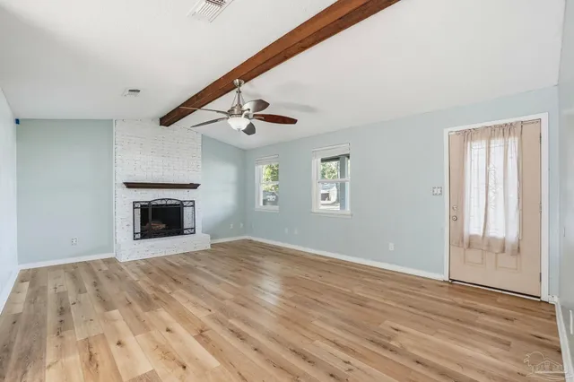 a view of an empty room with wooden floor fireplace and a window