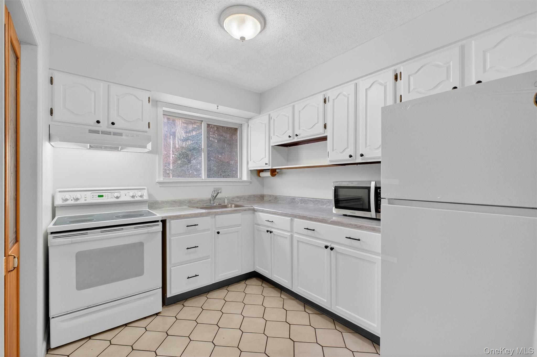 26 Cooper Road, Unit 715 Poughkeepsie, NY 12603 - Photo 16 of 30 Kitchen with white appliances, light countertops, white cabinets, a textured ceiling, and under cabinet range hood