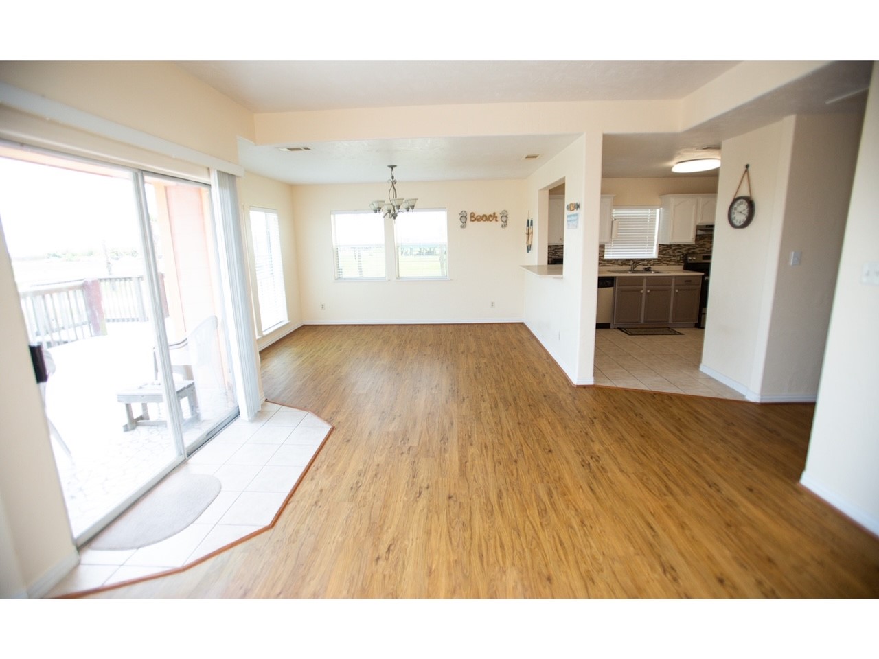 419 Thunder Road Surfside Beach, TX 77541 - Photo 11 of 32 Bright, open-concept living area with laminate wood flooring and ample natural light. Sliding glass doors lead to a patio, and the kitchen features modern tile and appliances. Ideal for entertaining.