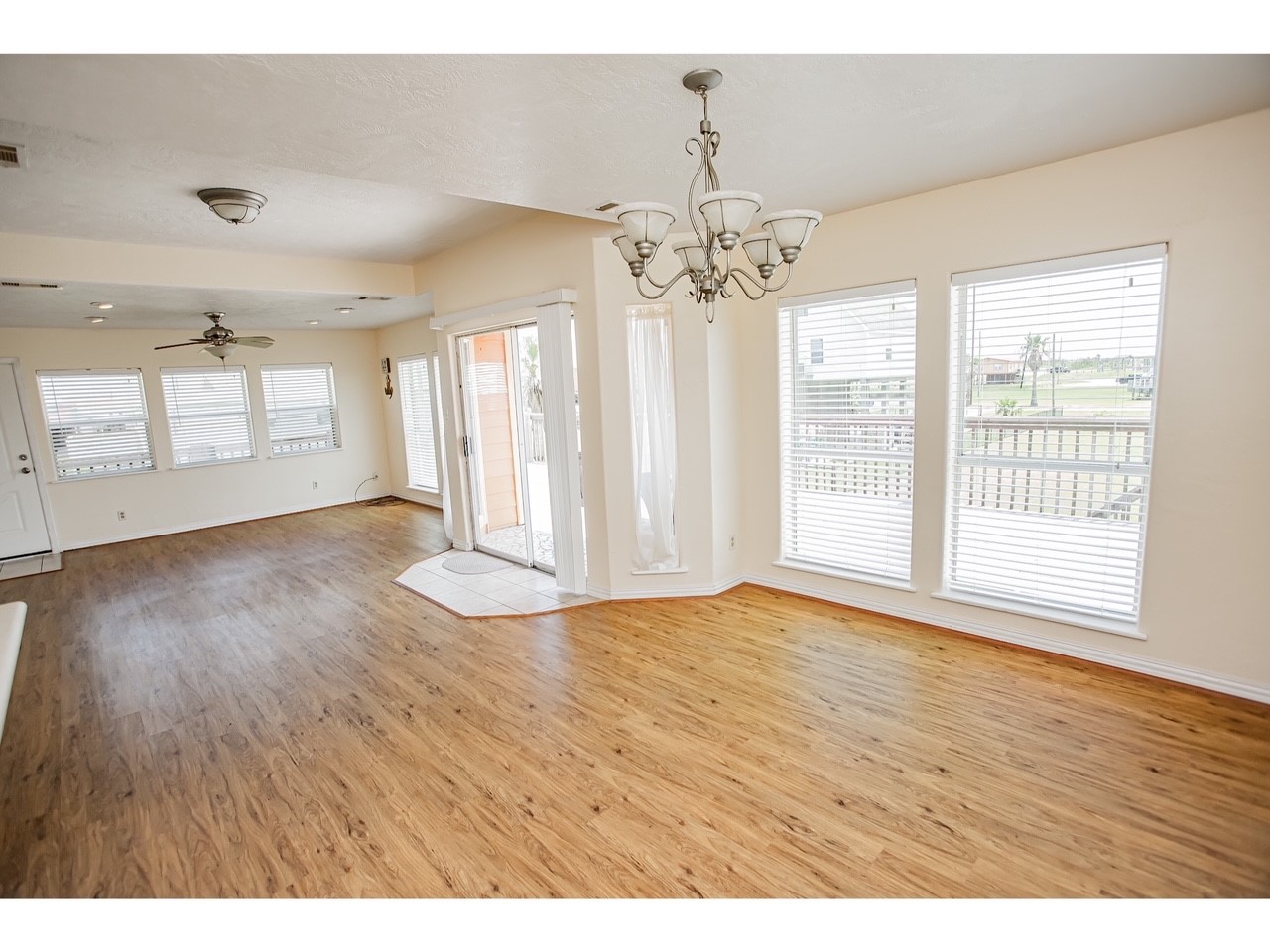 419 Thunder Road Surfside Beach, TX 77541 - Photo 12 of 32 This spacious, well-lit room features hardwood flooring, large windows with blinds for natural light, and a decorative chandelier. It opens to a patio through glass doors, offering a versatile living or dining area.