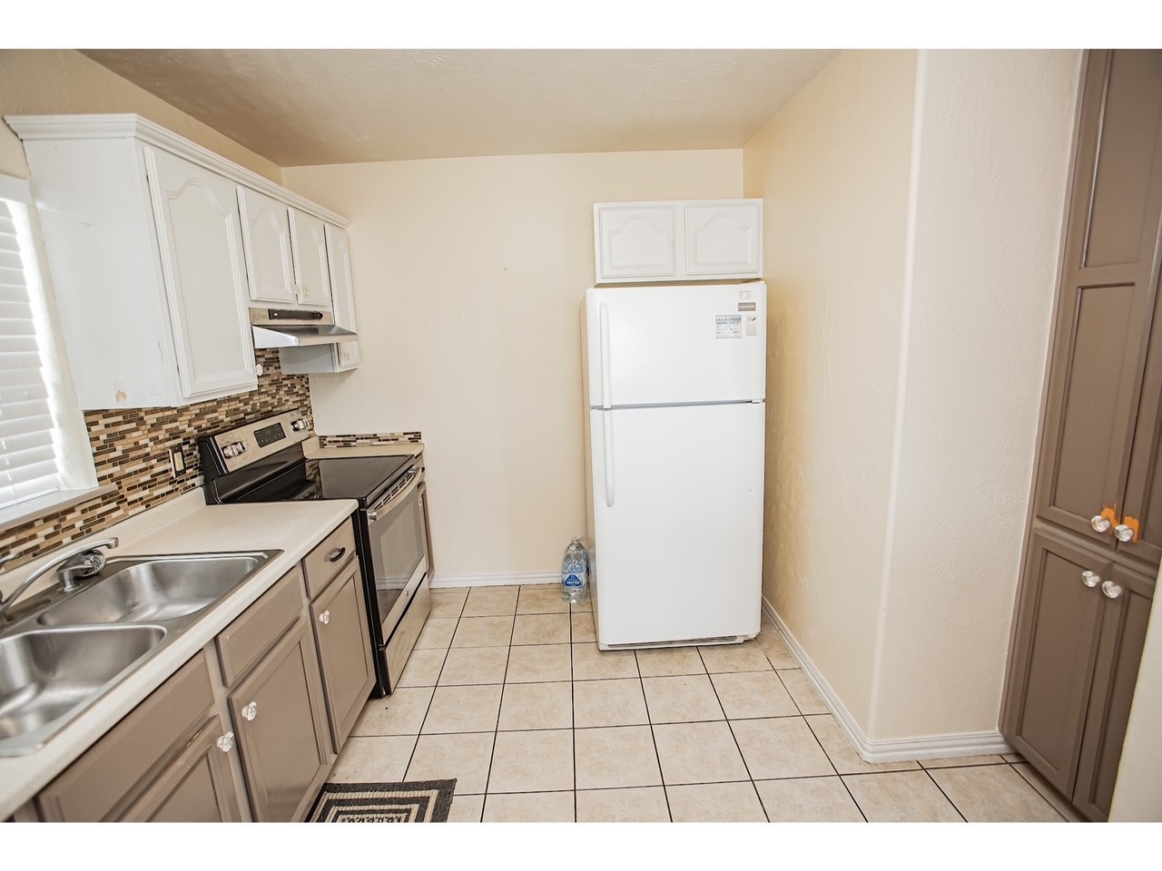 419 Thunder Road Surfside Beach, TX 77541 - Photo 15 of 32 This kitchen features tiled floors, white cabinetry, and a mosaic backsplash. It includes a double sink, stainless steel stove, and a white refrigerator, offering a compact but functional space.
