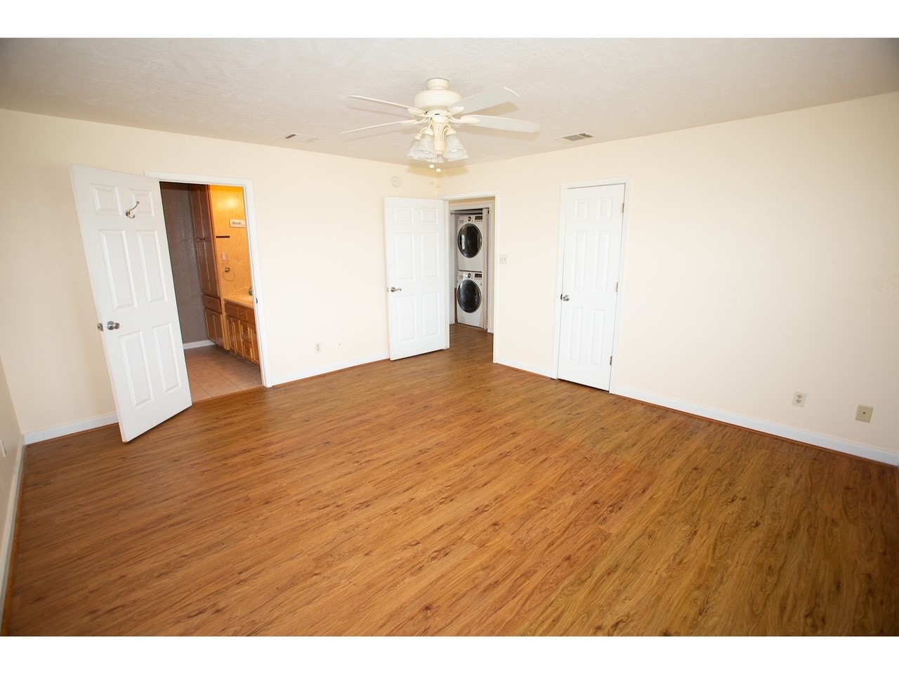 419 Thunder Road Surfside Beach, TX 77541 - Photo 22 of 32 Spacious room with wood flooring, ceiling fan, and neutral walls. Features include a doorway leading to a bathroom and a laundry area with a stacked washer and dryer.