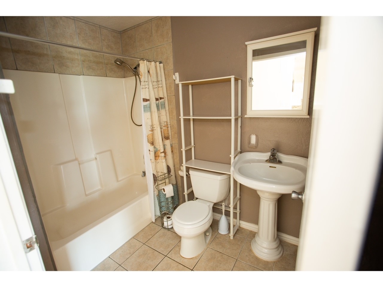 419 Thunder Road Surfside Beach, TX 77541 - Photo 23 of 32 Discover the cozy master bathroom, featuring a clean, modern design with a convenient shower-tub combo, elegant pedestal sink, and practical storage shelving.
