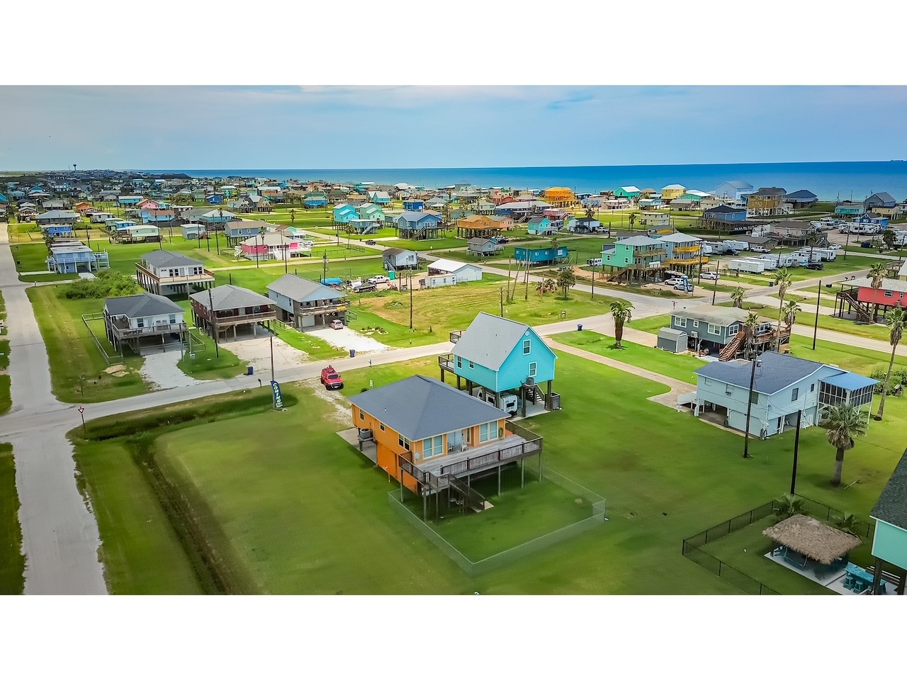 419 Thunder Road Surfside Beach, TX 77541 - Photo 29 of 32 This photo shows a coastal neighborhood with colorful elevated homes, spacious green lawns, and proximity to the ocean, offering a vibrant and scenic living environment.