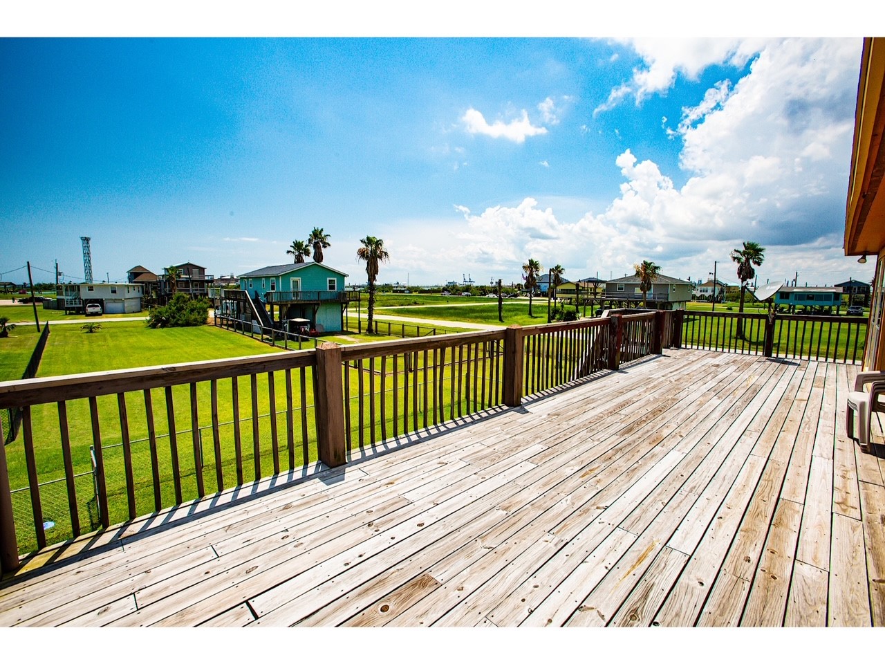 419 Thunder Road Surfside Beach, TX 77541 - Photo 8 of 32 This photo showcases a spacious wooden deck with a view of a grassy yard and neighboring houses, set against a bright sky with a few clouds. Ideal for outdoor relaxation and entertaining.