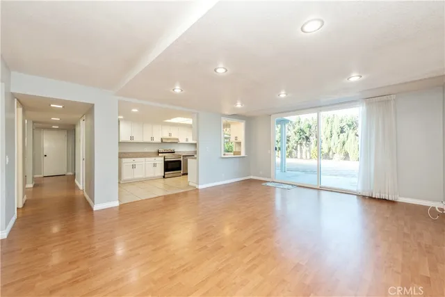a view of an empty room and a kitchen with wooden floor