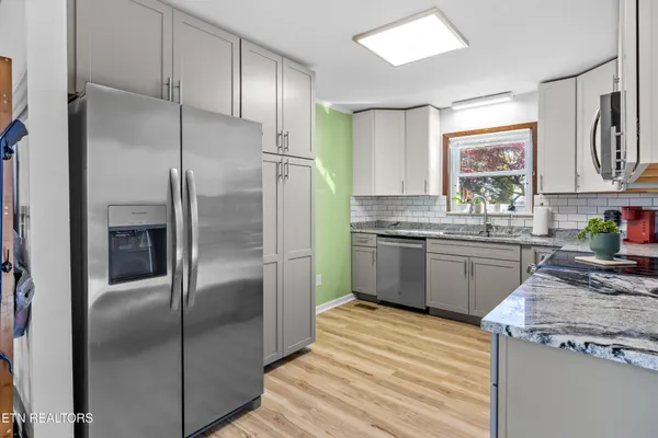 a kitchen with stainless steel appliances granite countertop a refrigerator a sink a stove and white cabinets with wooden floor