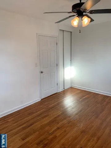 a view of an empty room with wooden floor fan and window