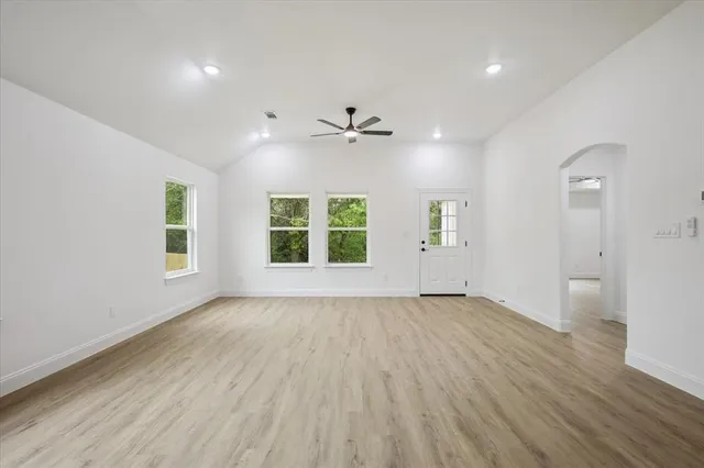 an empty room with wooden floor chandelier fan and windows