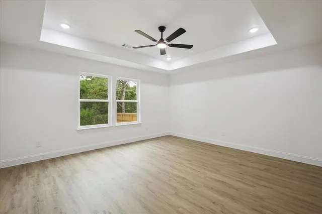 an empty room with wooden floor a ceiling fan and windows