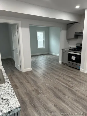 an empty room with wooden floor kitchen view and windows