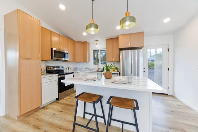 a kitchen with stainless steel appliances kitchen island granite countertop a refrigerator a stove a sink dishwasher and a dining table with wooden floor