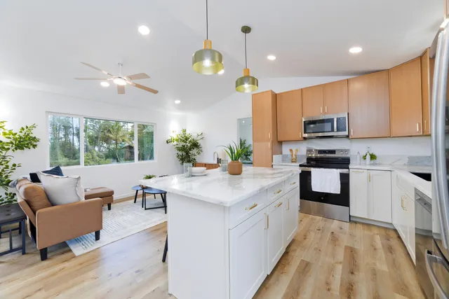 a kitchen with stainless steel appliances kitchen island granite countertop a stove a sink dishwasher and white cabinets with wooden floor