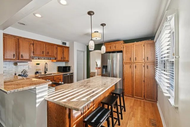 a kitchen with stainless steel appliances granite countertop a refrigerator a sink dishwasher a stove and white cabinets with wooden floor