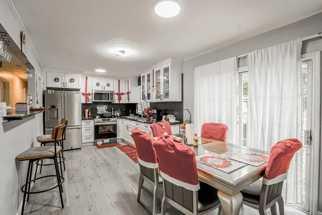 a dining room with stainless steel appliances kitchen island granite countertop a dining table chairs and a refrigerator
