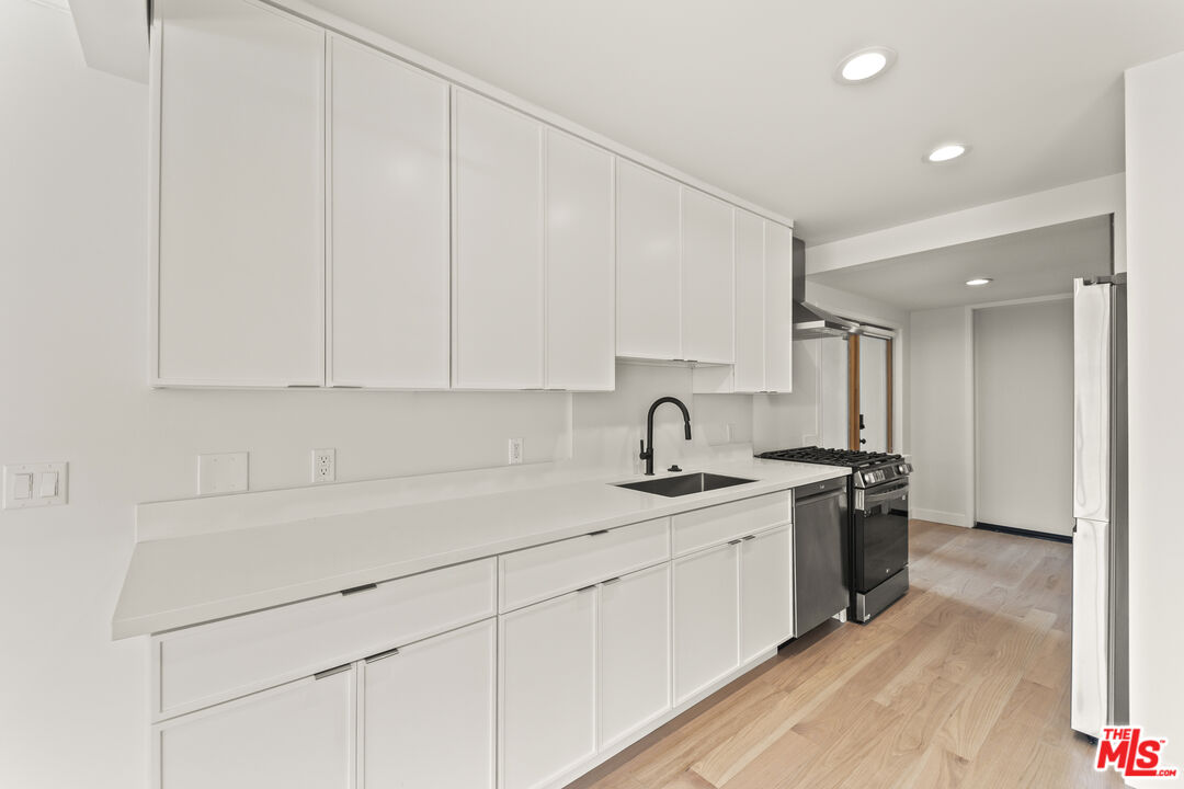751 18th Street, Unit B Santa Monica, CA 90403 - Photo 9 of 24 a kitchen with a sink dishwasher and white cabinets with wooden floor