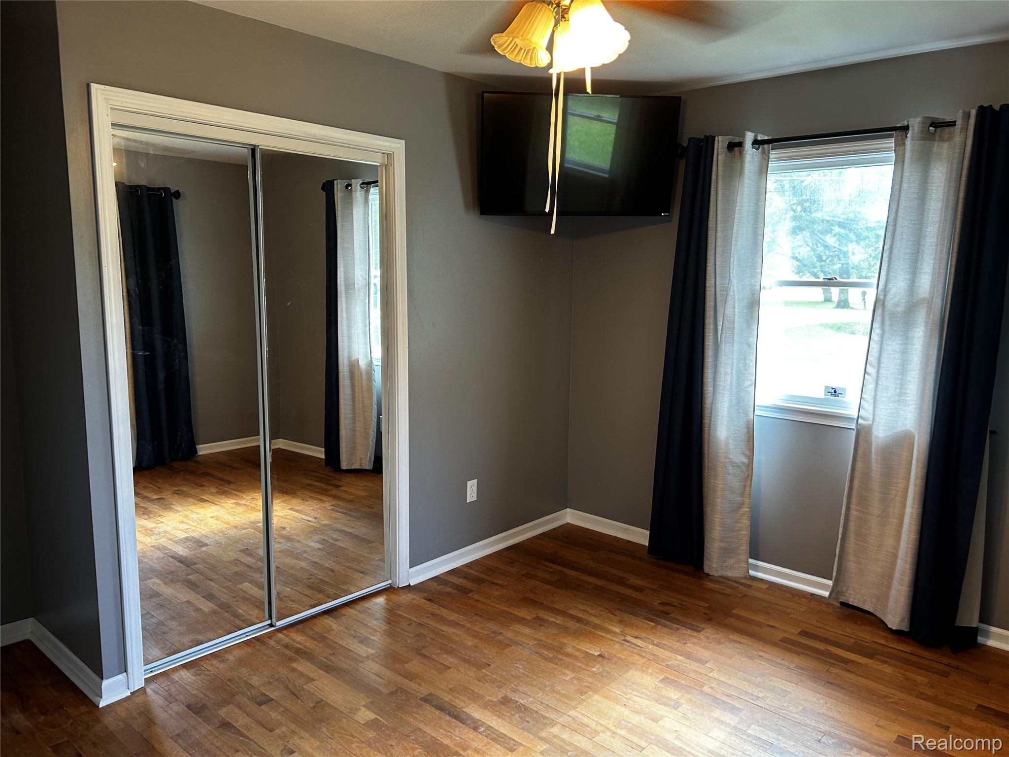 5440 Deland Road Flushing, MI 48433 - Photo 12 of 25 Main Bedroom featuring wood-finish flooring, mirrored sliding closet doors, and a ceiling fan with integrated lighting.