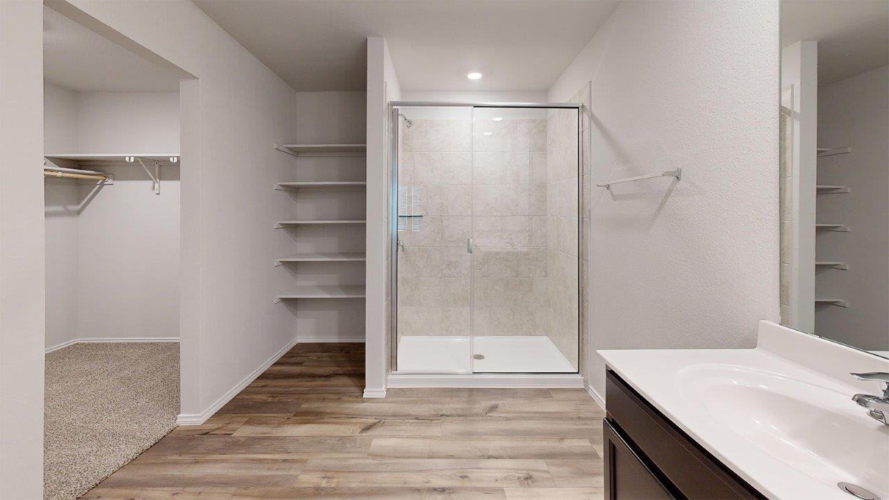 557 Hector Loop Georgetown, TX 78626 - Photo 27 of 38 Glass-enclosed shower with tiled surround, wood-finish flooring, built-in shelving, and a vanity with a white countertop