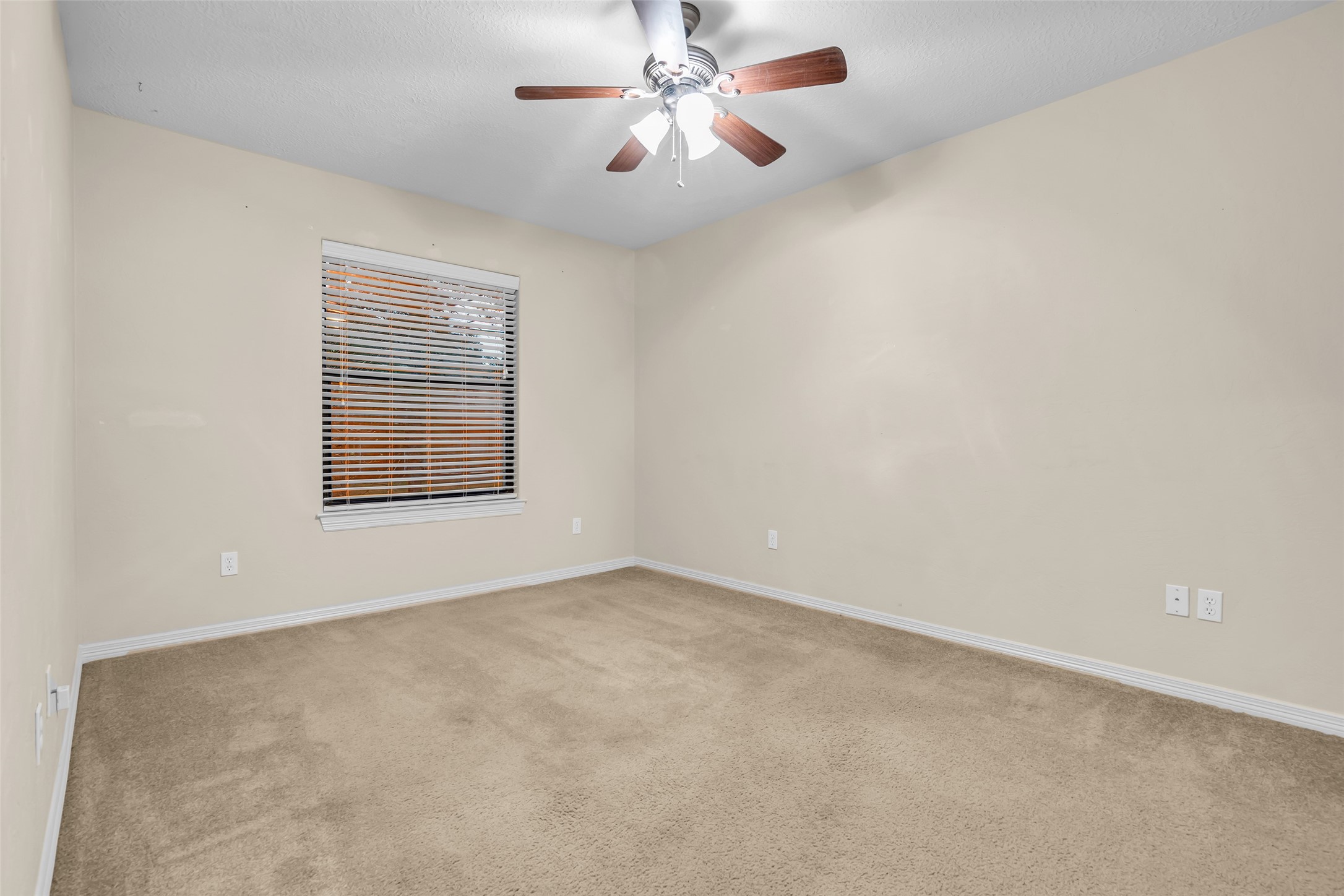 1898 Longmire Road, Unit 5 Conroe, TX 77304 - Photo 38 of 48 This room is cozy with neutral-colored walls and carpet, featuring a ceiling fan with lights. A window with blinds allows natural light in, creating a comfortable living space.