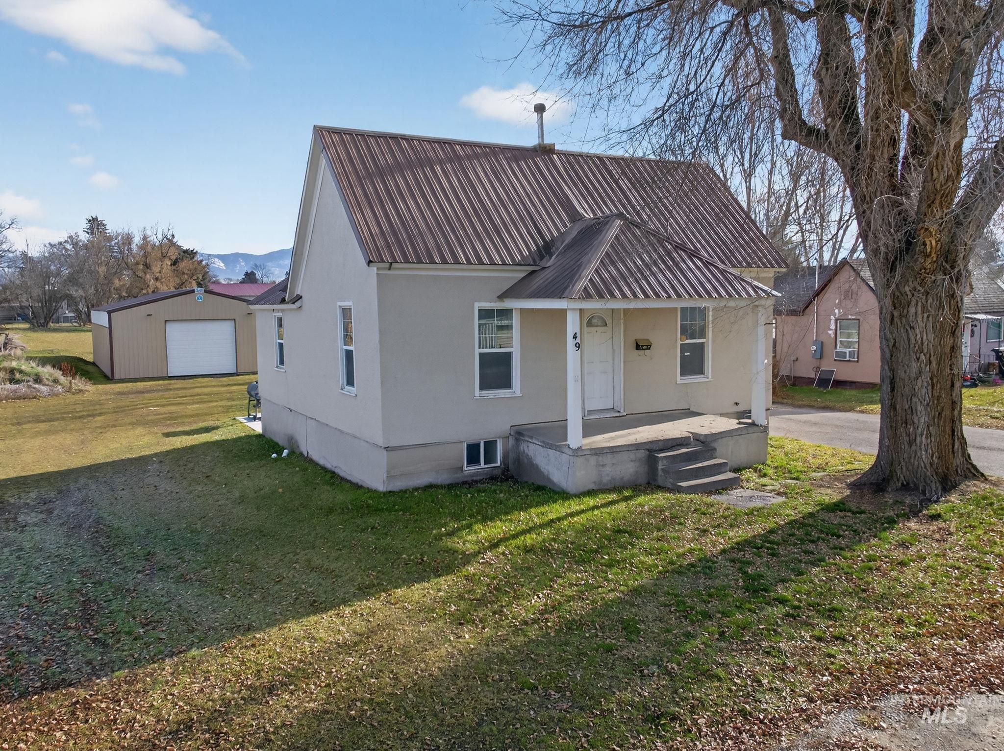 View of front of property with a front lawn, a porch, an outdoor structure, a metal roof, and stucco siding