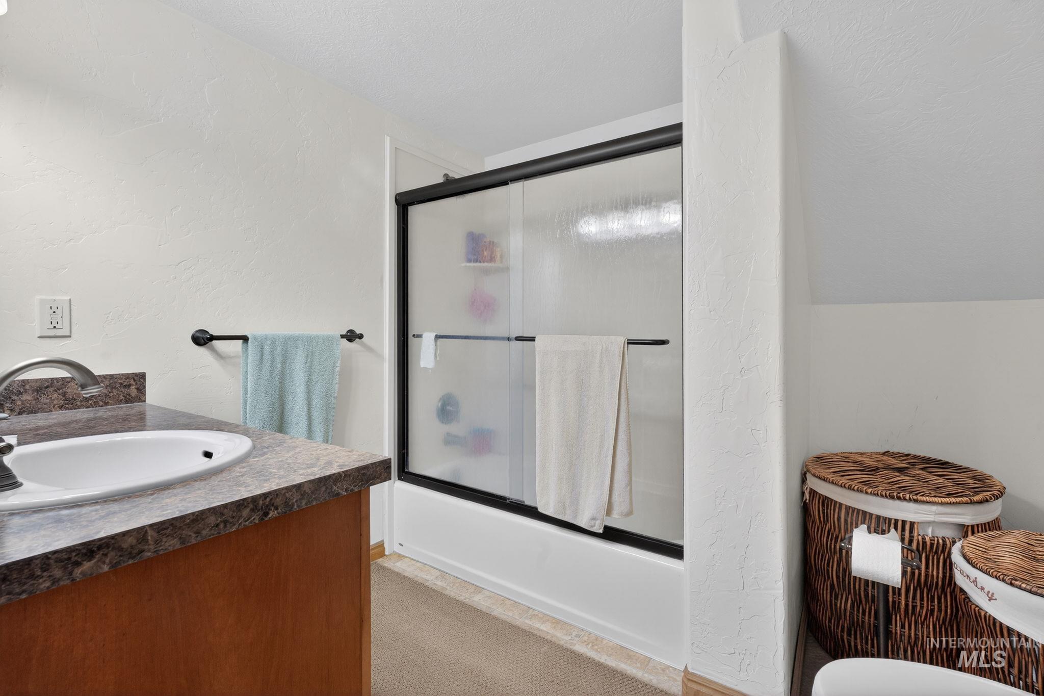 49 South 4th Street West Preston, ID 83263 - Photo 16 of 48 Bathroom featuring a textured wall, bath / shower combo with glass door, vanity, and a textured ceiling