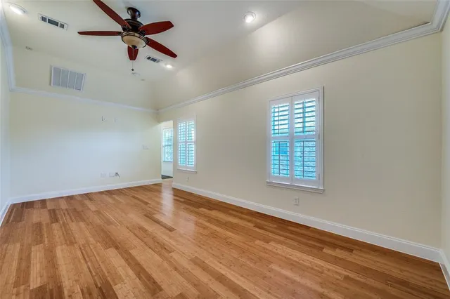 an empty room with wooden floor fan and windows