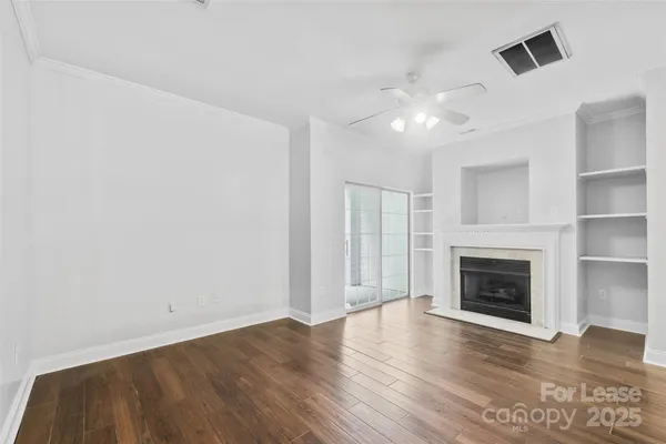a view of an empty room with wooden floor fireplace and a window