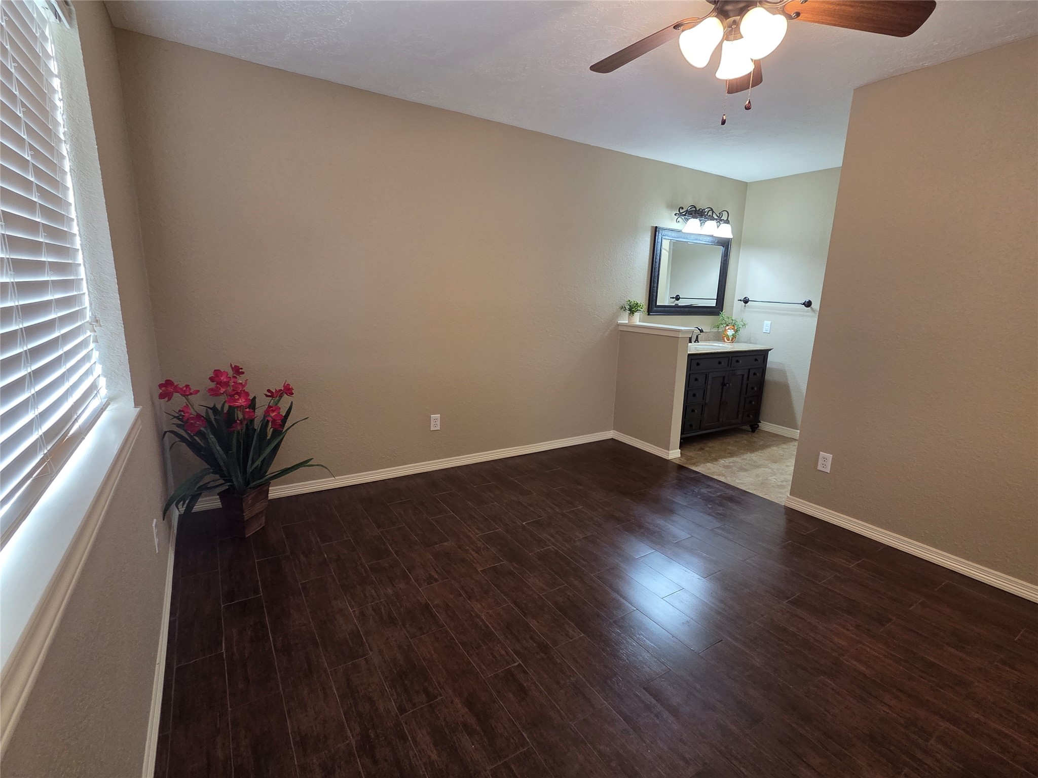 4203 Spinks Creek Lane Spring, TX 77388 - Photo 9 of 14 The primary bedroom features dark wood flooring, neutral walls, and a ceiling fan. It includes a cozy nook with a vanity and mirror, and a window that lets in natural light, enhancing the spacious feel.