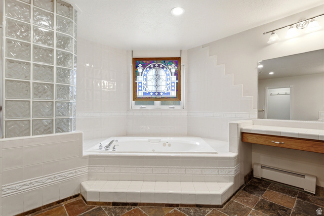 3535 Homestead Road Park City, UT 84098 - Photo 43 of 81 White tiled bath area featuring a built-in jetted tub, a stained-glass window, a glass block shower enclosure, a vanity with a wood-finish base, and slate-style floor tiling