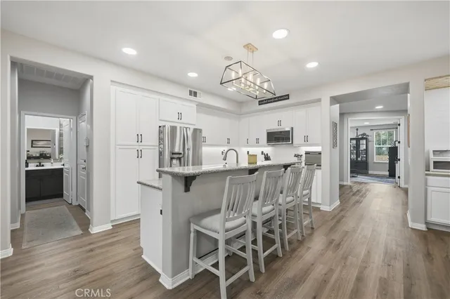 a kitchen with stainless steel appliances granite countertop a refrigerator a sink dishwasher a stove and white cabinets with wooden floor