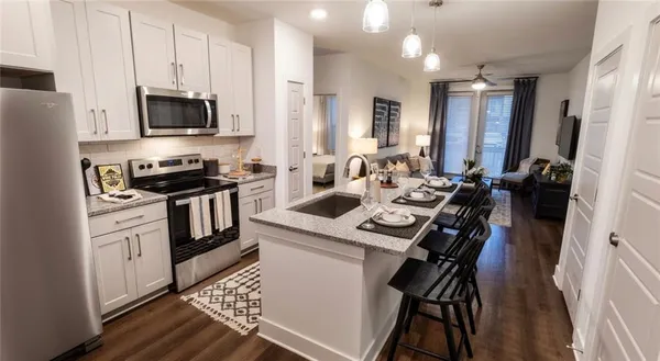 a kitchen with stainless steel appliances a stove a sink dishwasher a microwave oven a refrigerator with white cabinets and wooden floor