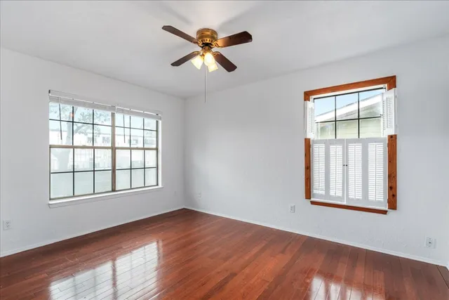 an empty room with wooden floor fan and windows