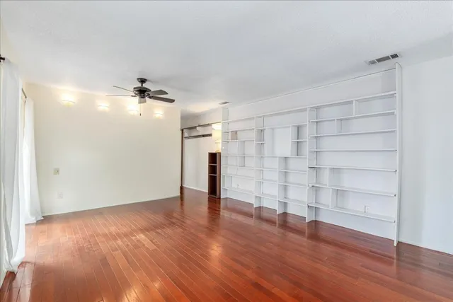 a view of empty room with wooden floor and fan
