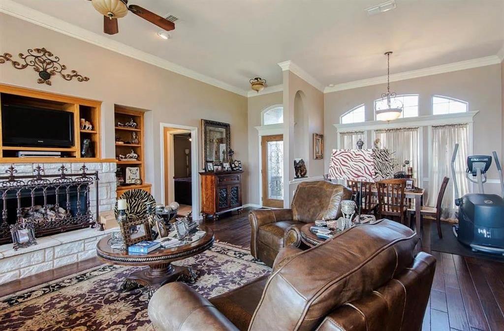 10899 Jackson Road Krum, TX 76249 - Photo 4 of 11 Living room with hardwood / wood-style flooring, a stone fireplace, crown molding, a ceiling fan, and built in shelves