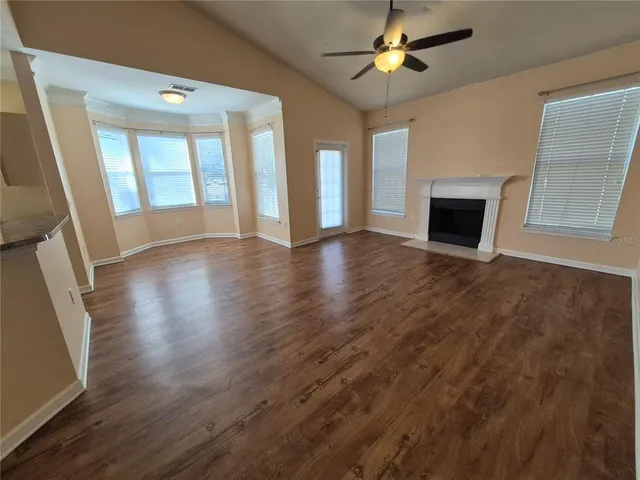 an empty room with wooden floor fireplace and windows