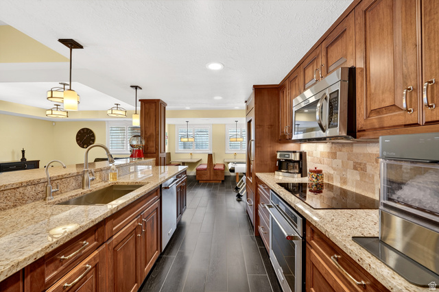 714 Draper Heights Way Draper, UT 84020 - Photo 52 of 88 Kitchen featuring wood finish cabinets, light stone counters, stainless steel appliances, pendant lighting, and dark wood-style flooring