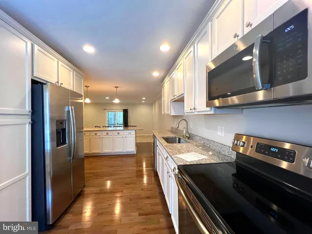 a kitchen with stainless steel appliances granite countertop a refrigerator a stove and a sink with wooden floor