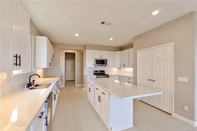 a large white kitchen with stainless steel appliances granite countertop a lot of counter space and wooden floors