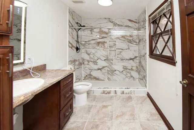 a bathroom with a granite countertop sink a toilet and shower