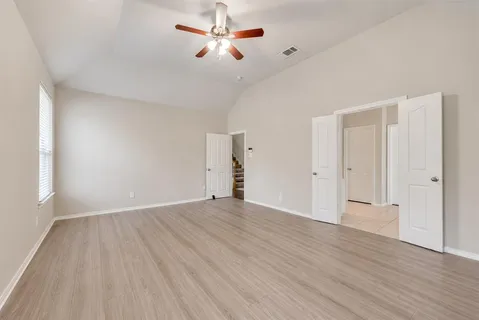 an empty room with wooden floor chandelier fan and windows